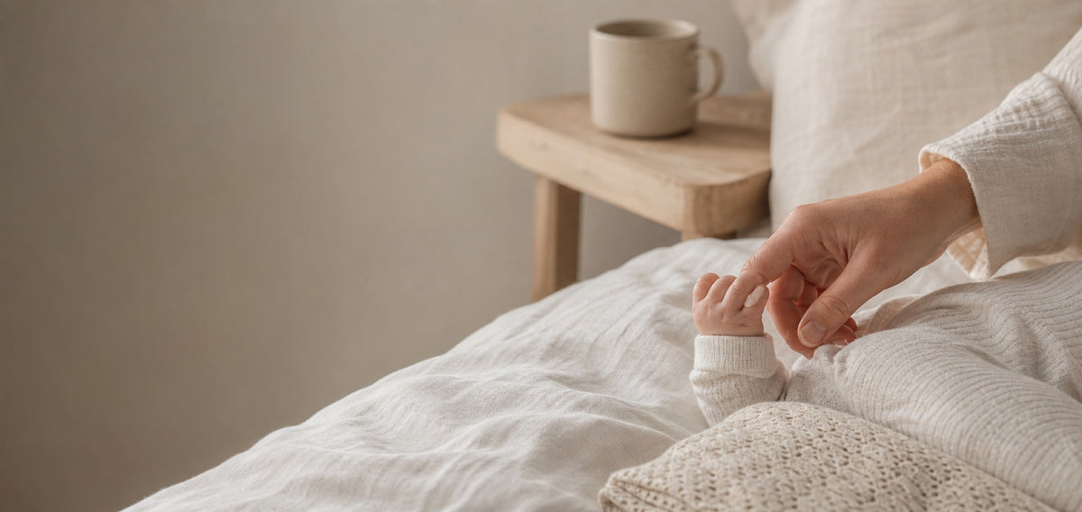 A baby's hand holding a mother's finger in soft morning light